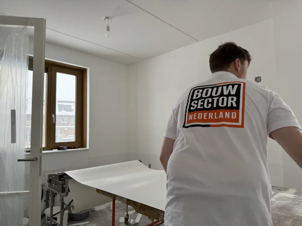 Behanger van Bouwsector Nederland legt een baan behang over de plaktafel in een nieuwbouwkamer