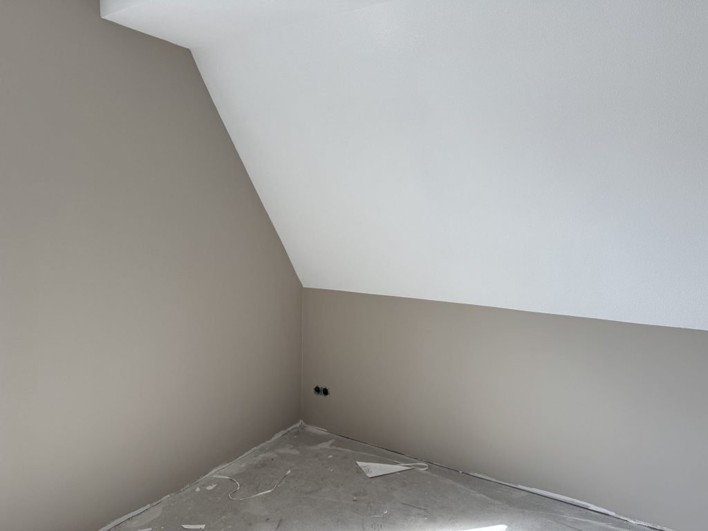 Zolderkamer met een schuine wand, lichtgrijze muren en een wit schuin plafond