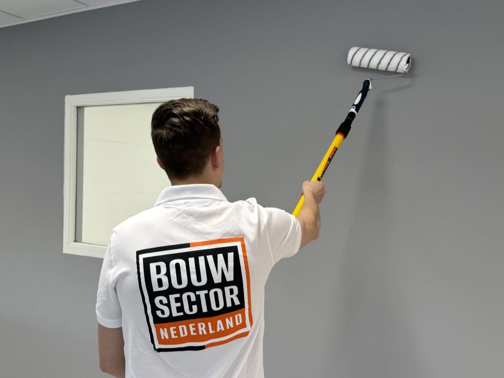 Schilder van Bouwsector Nederland rolt een grijze muur met een roller aan een gele verlengsteel
